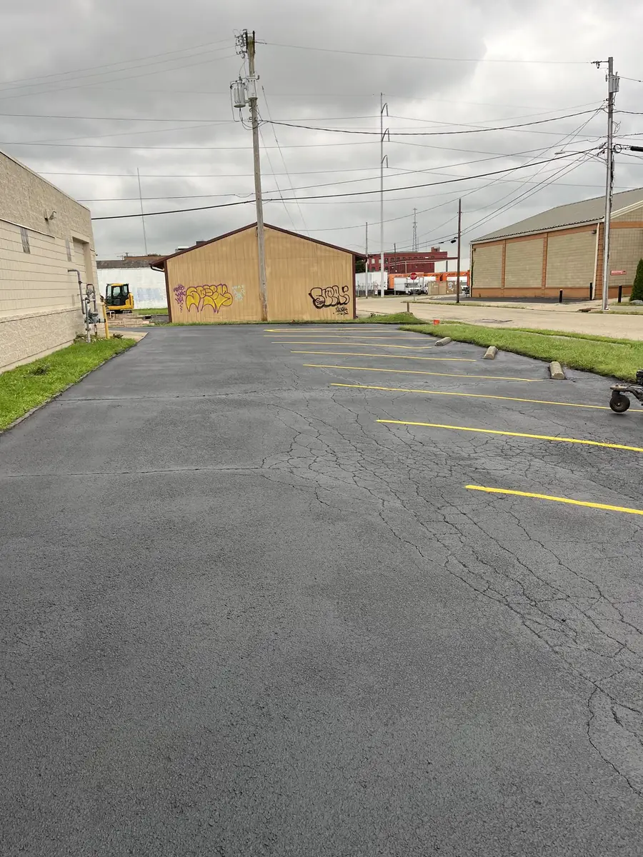 The same parking lot after sealcoating, with a uniform dark surface and fresh yellow stall striping